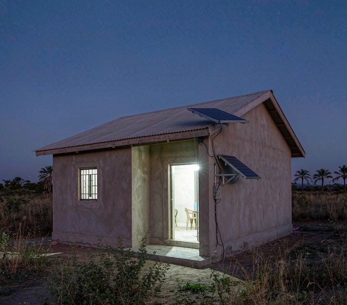 Rural home with solar panels mounted on the roof and wall, warm interior light glowing — AI-generated illustrative scene
